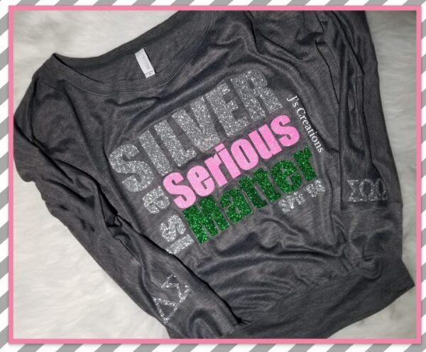 A gray long-sleeve shirt with the phrases "Silver & Serious Matter" printed in sparkly silver, pink, and green letters. The sleeves are also decorated with silver elements.