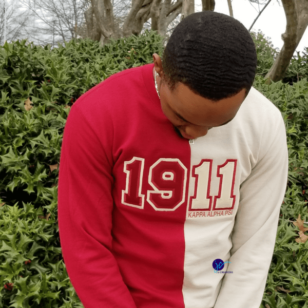 A person wearing an Embroidered 1911 Kappa Alpha Psi Inspired Half and Half Crew Neck Unisex Sweatshirt, standing outdoors with greenery and tree branches in the background.