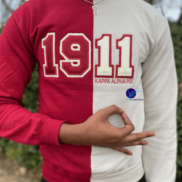 A person wearing an Embroidered 1911 Kappa Alpha Psi Inspired Half and Half Crew Neck Unisex Sweatshirt, making a hand gesture with their fingers.