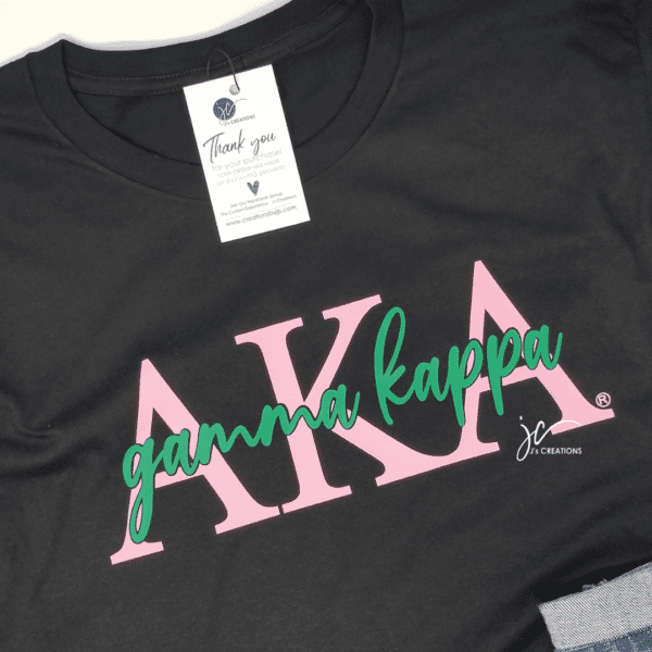 A black AKA Chapter Tee with pink Greek letters "AKA" and the text "gamma kappa" in green script. A tag attached to the shirt reads "Thank you for your purchase!".