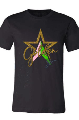 A black Golden Soror Ladies Fitted Tee featuring a glittery gold star design with the word "Golden" written across it. The star encompasses pink and green segments with a stylized signature below.