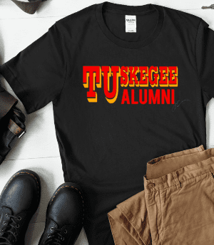 A black Tuskegee Family Member Unisex Shirt (Father, Mother, Sister, etc.) is laid out alongside brown pants, black boots, a leather bag, a smartphone, and a notebook on a white surface.