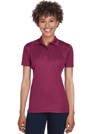 A person with short curly hair is smiling while wearing a short-sleeved, maroon Tuskegee Ladies Polo with TU Tiger Scratch Embroidery Design and dark pants, standing against a plain white background.