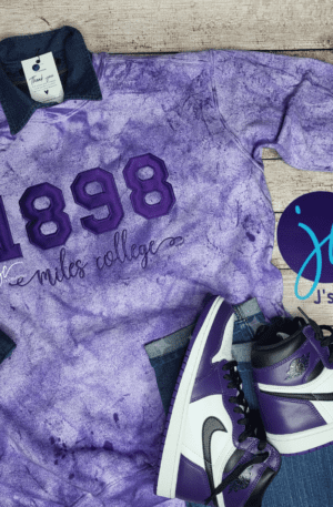 A purple tie-dye shirt with "1898 Miles College" text, paired with white and purple sneakers. A logo with "jc J's Creation" is visible on the right side, celebrating the elegance of an 1881 Tuskegee University Colorblast Unisex Embroidered Sweatshirt.