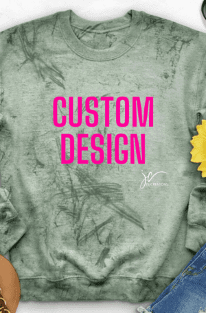 Green Custom Colorblast Unisex Embroidered Sweatshirt with "Custom Design" in bold pink letters, lying flat with a pair of sunglasses, a sunflower, a pair of sandals, and denim shorts placed around it. Perfect for an Alpha Kappa Alpha Soror Shirt look!