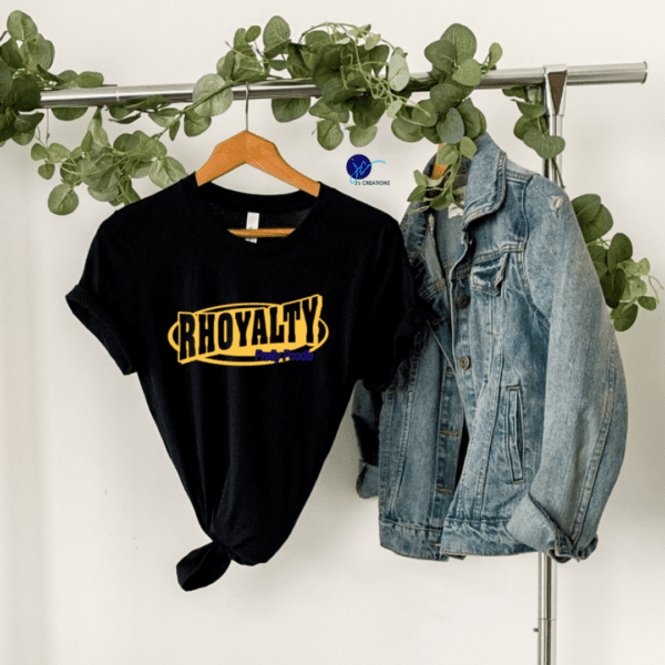 A Rhoyalty Pretty Poodle Unisex Tee hangs next to a denim jacket on a clothing rack adorned with green leaves.